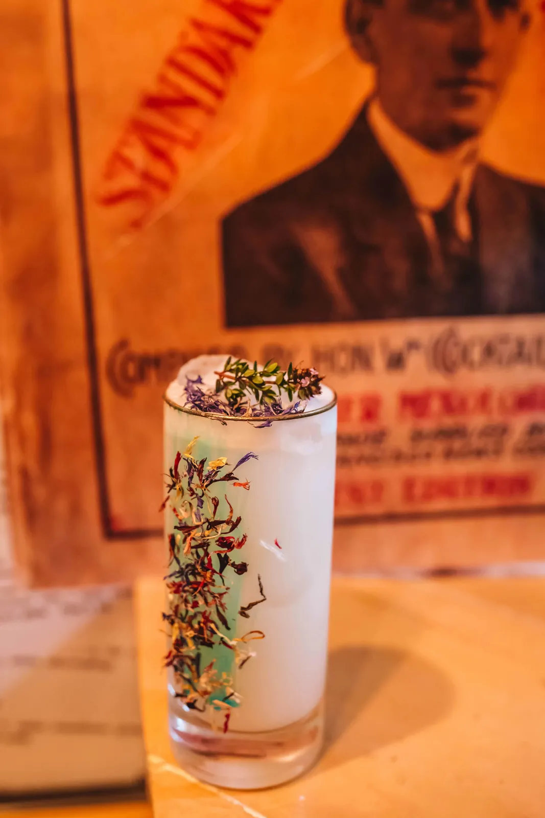 Cocktail bianco in un bicchiere alto, decorato con fiori secchi e timo